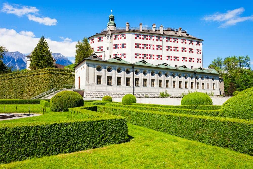 Ambras Castle: Skip The Line Manicured gardens with hedges, topiaries, and a large building in the background under a clear blue sky.