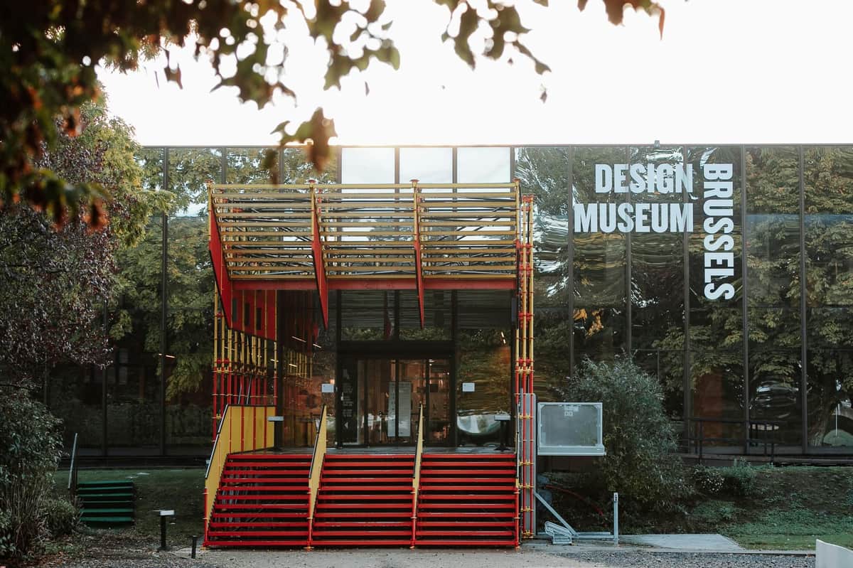 Design Museum Brussels: Skip The Line Ticket Entrance of a modern Design Museum building with red and yellow stairs, a glass facade, and greenery around.