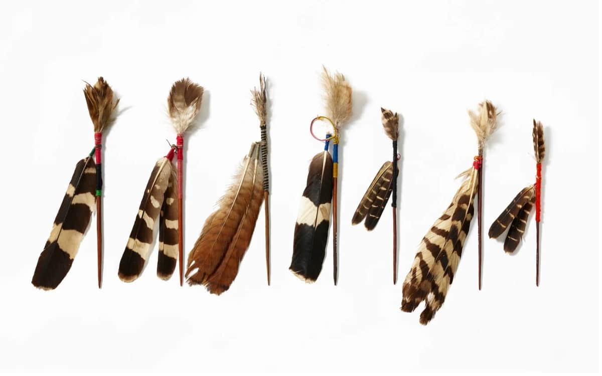 Royal Ontario Museum Feature Exhibit: Pyschedelics A row of decorative feather arrangements tied to small sticks against a white background.