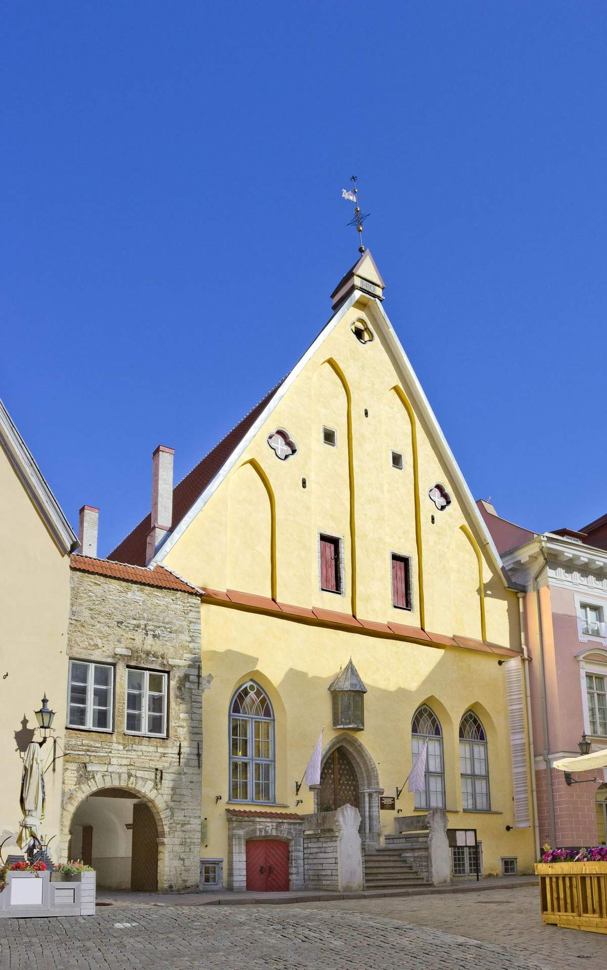 Great Guild Hall: Skip The Line Ticket A medieval building with a yellow facade, arched windows, small attic windows, and a weather vane, set against a clear blue sky.