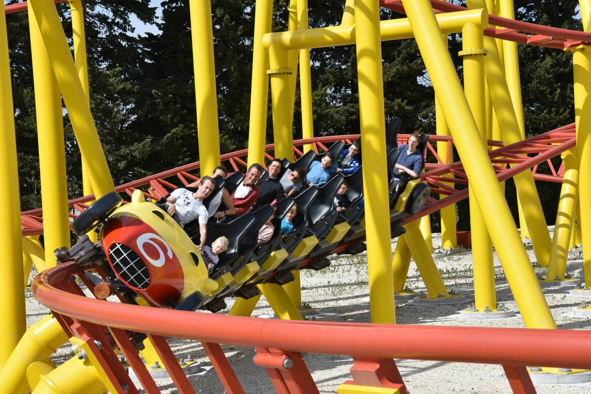 Parc Spirou Provence: Early Bird Fast Track Ticket People riding a yellow and red rollercoaster with loops and turns, surrounded by trees.