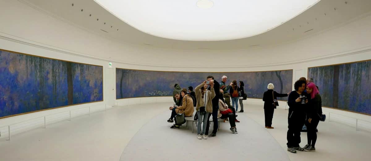 Musée de l'Orangerie: Small Group Guided Tour in English People observing a large panoramic painting in a museum gallery with a white curved ceiling and benches in the center.