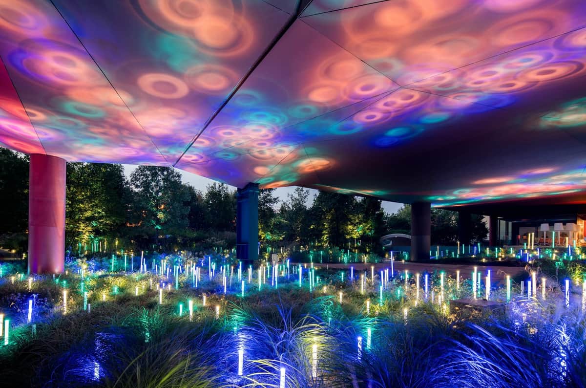 Musée du quai Branly - Jacques Chirac: Skip The Line Annual Pass An outdoor light installation featuring colorful, illuminated rods and circular projections on a canopy, surrounded by trees and foliage.