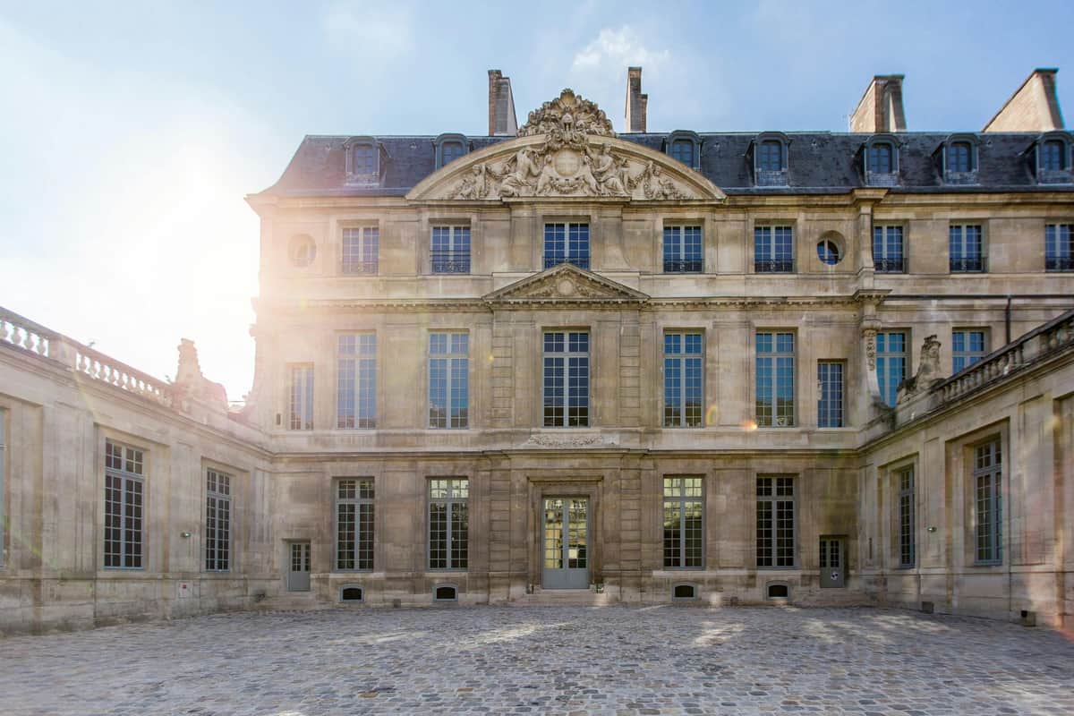 Musée national Picasso-Paris: Priority Entry Ticket A historic stone building with tall windows, ornate detailing, and a cobblestone courtyard, under a bright sky.