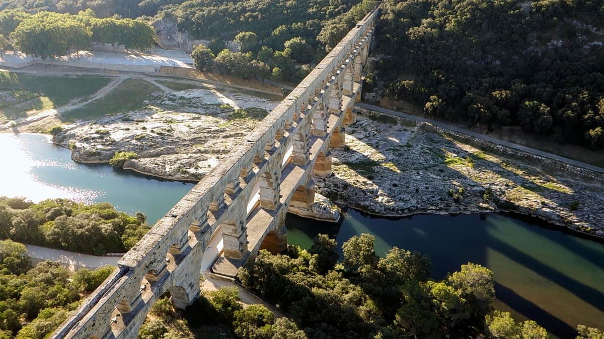 Pont du Gard + Museum: Skip The Line Ancient stone aqueduct spanning a river, surrounded by trees and rocky terrain.