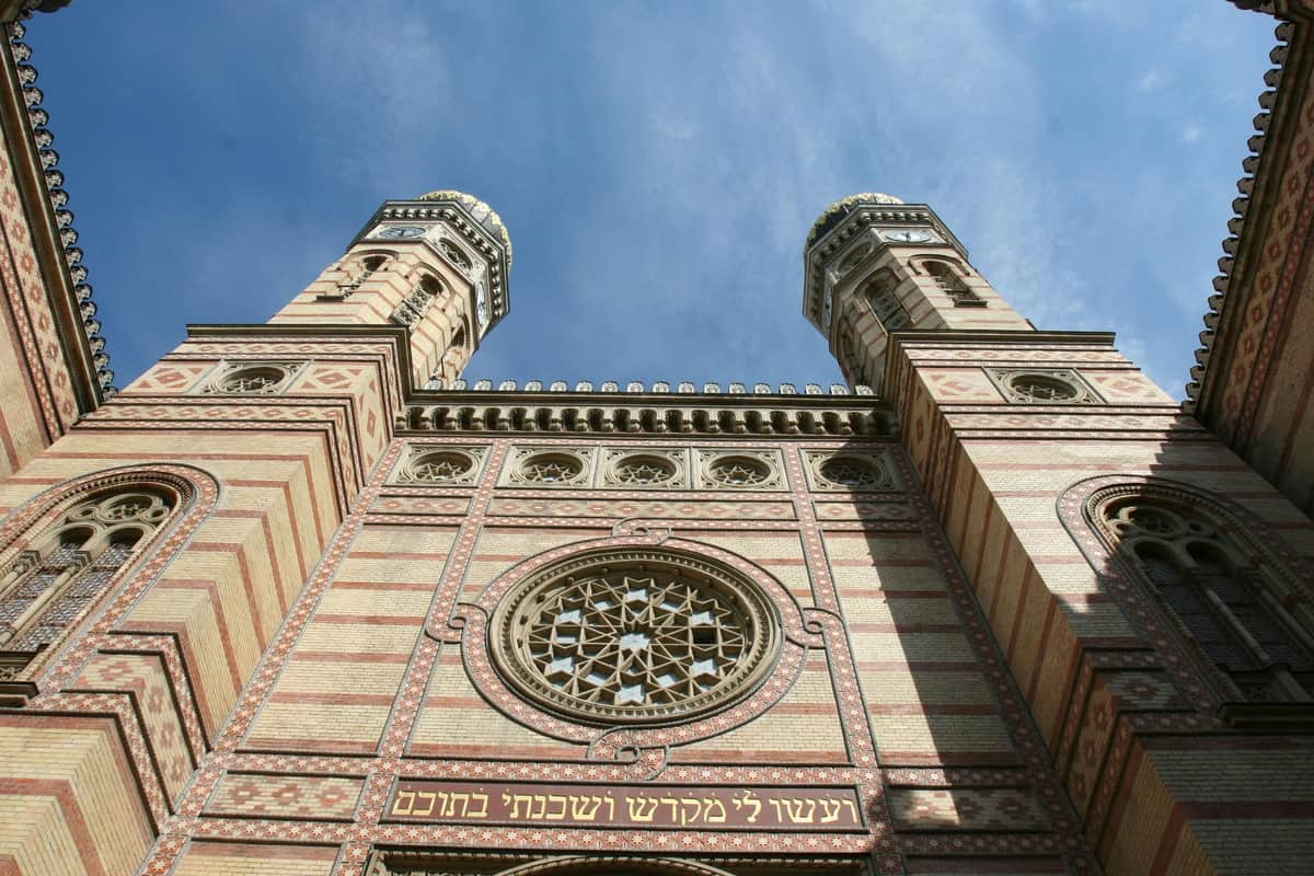 Great Synagogue + Jewish Quarter Walking Tour Ornate building facade with two tall towers, a circular stained glass window, and decorative Hebrew inscriptions, under a blue sky.