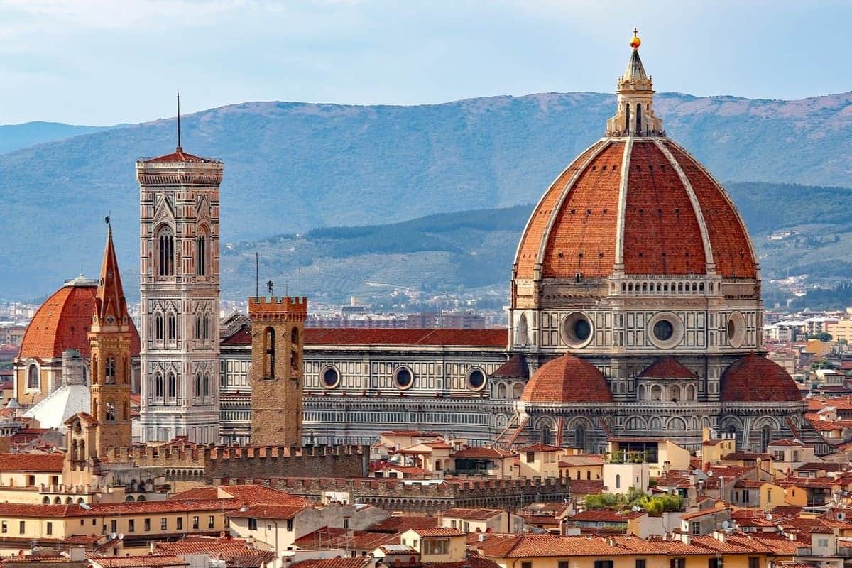 A panoramic view of Florence's Cathedral of Santa Maria del Fiore with its red dome and bell tower, surrounded by rooftops.