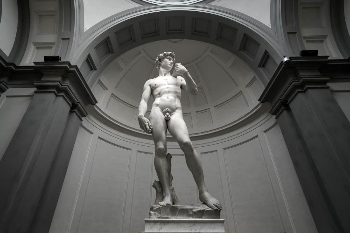 Accademia Gallery: Priority Entry Ticket A white marble statue of a nude male in a grand, domed indoor setting with ornate architectural details.