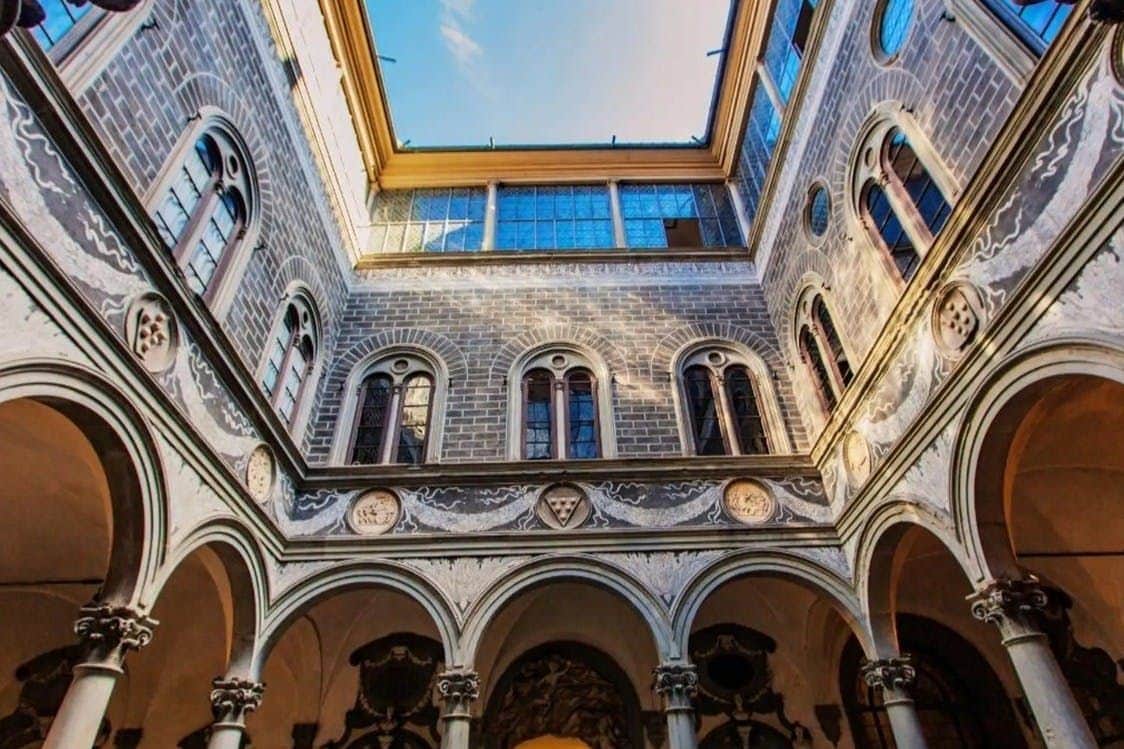 Interior courtyard of a historic building with arched windows, intricate stonework, and an open view of the blue sky above.