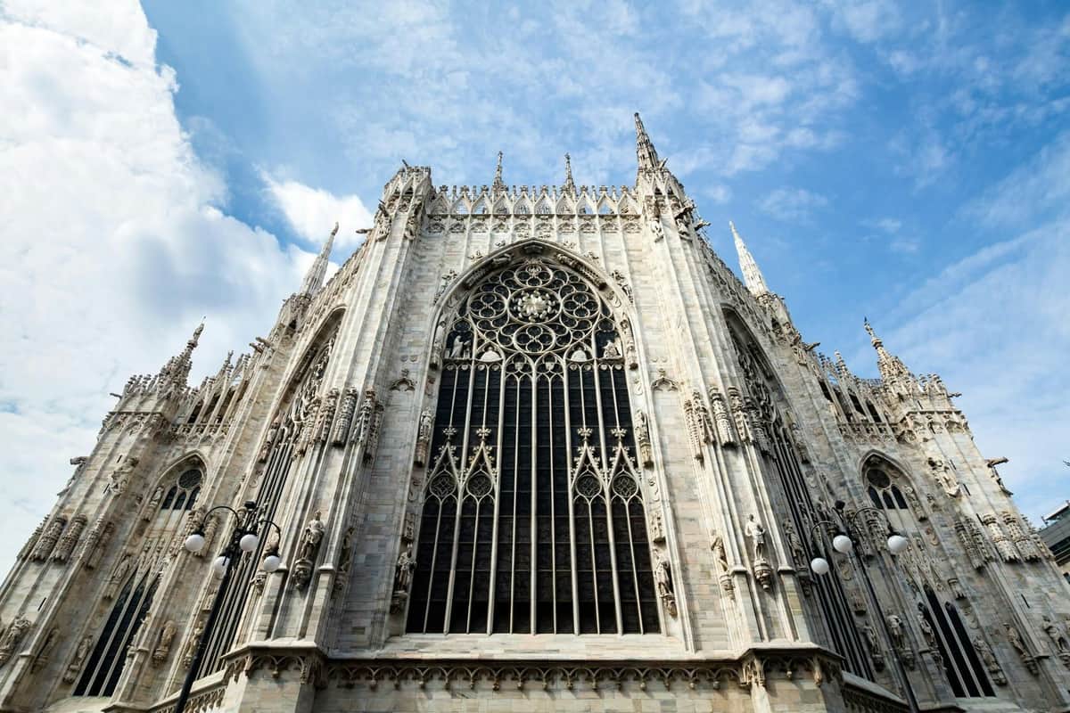 A detailed Gothic cathedral facade with intricate carvings and pointed arches, under a partly cloudy blue sky.