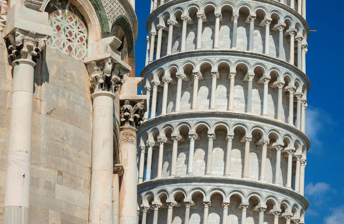Close-up of detailed architectural columns and arches of leaning tower against clear blue sky.