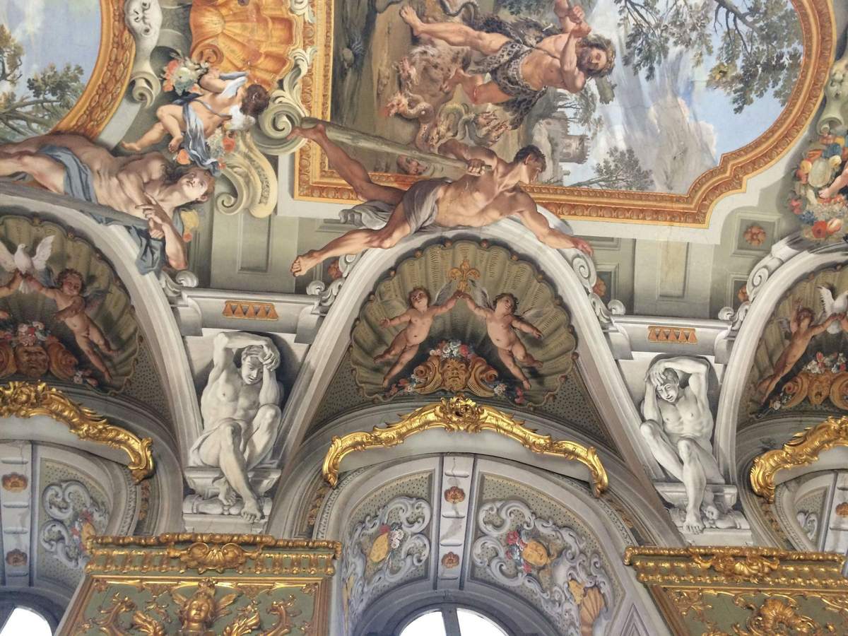 Palazzo Doria Pamphilj: Skip The Line Ticket An ornate ceiling with intricate frescoes featuring mythological figures and cherubs, framed by decorative arches and gilded accents.