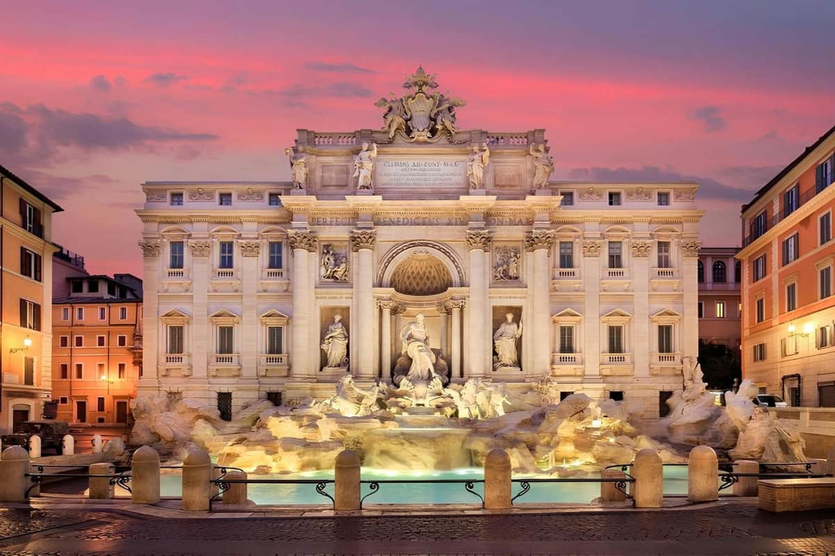 The Trevi Fountain in Rome, illuminated at sunset, featuring ornate sculptures and a pool of water in the foreground.