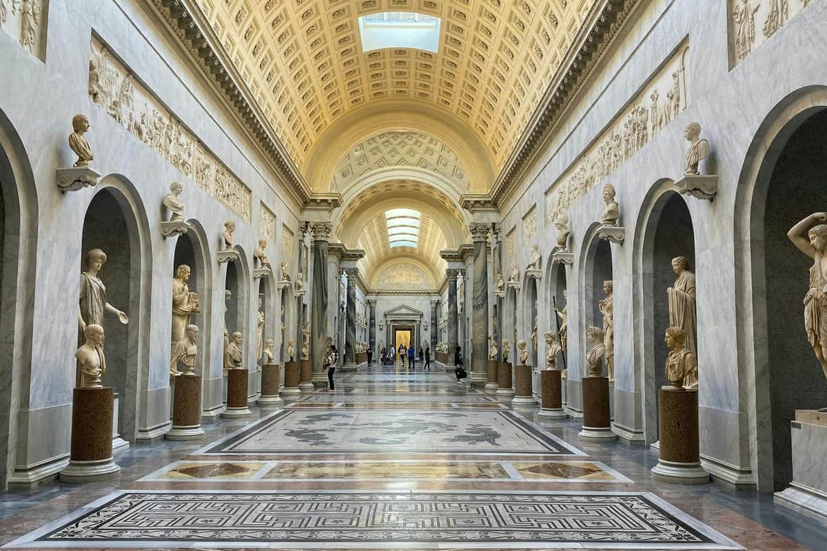 Vatican Museums & Sistine Chapel: Guided Tour + Priority Entry A grand hall with ornate arched ceilings, statues in niches along the walls, and a patterned floor, in a museum setting.