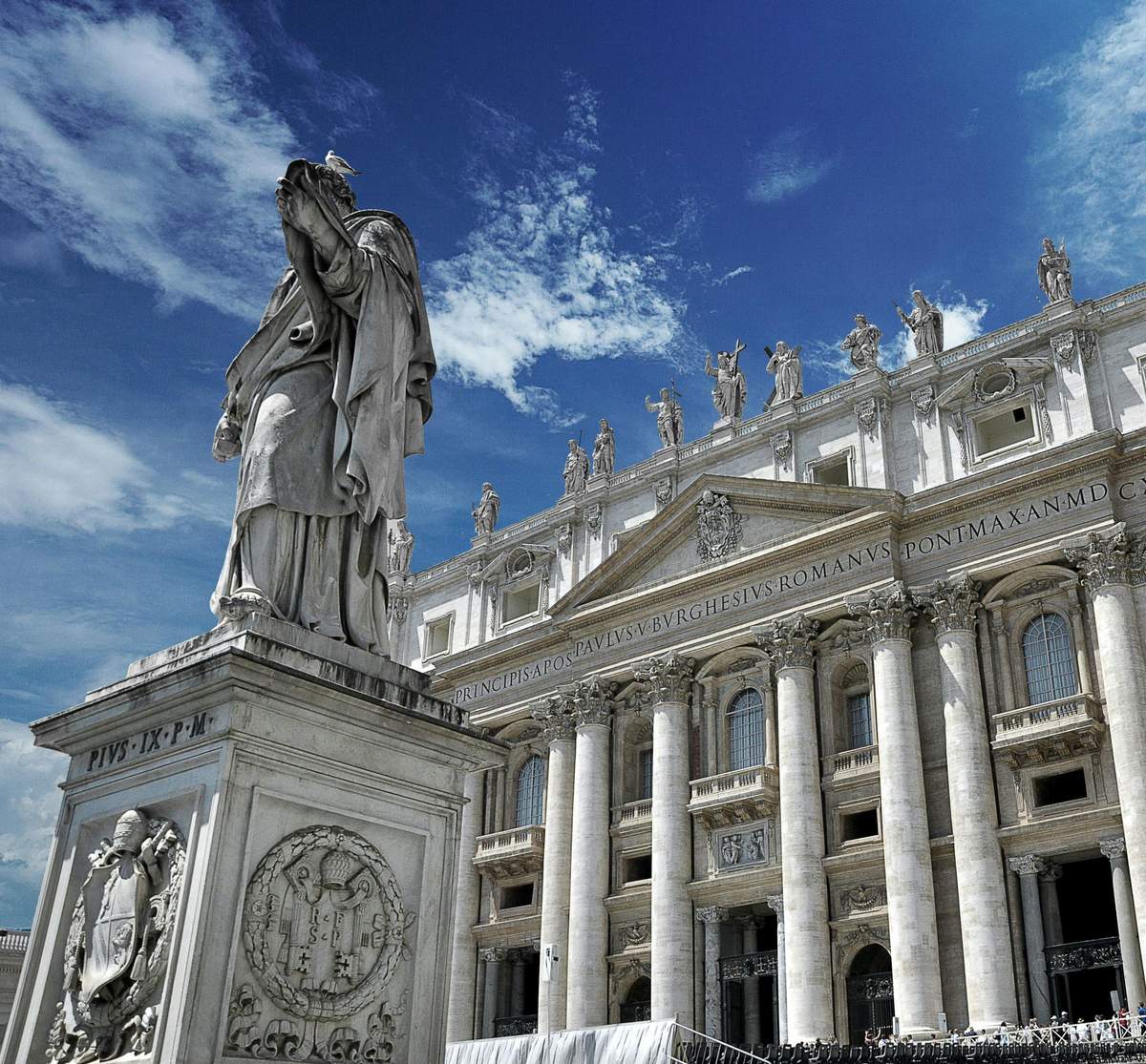 Vatican Museums & Sistine Chapel: Guided Tour A marble statue in front of an ornate building with columns and statues on the rooftop, under a blue sky with clouds.