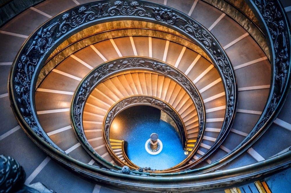 Vatican Museums & Sistine Chapel: Multi-Attraction Combo Pass Intricate spiral staircase with decorative railing and steps leading down to a bright blue circular floor and a central pedestal.