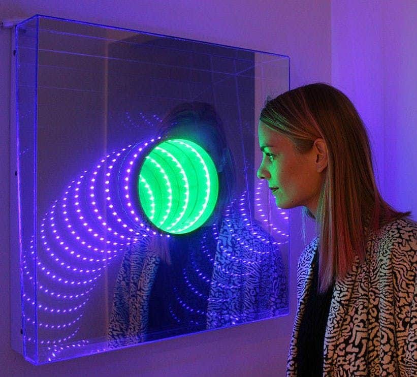Cosmos Illusion Museum: Skip The Line Ticket A woman looks closely at a colorful light art installation with green and purple LED lights in a mirrored setup.