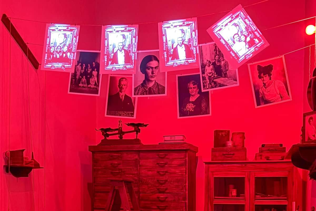 Casa Kahlo: Skip The Line Entry A room lit in red with vintage photos hanging, a wooden cabinet, and an old-fashioned weighing scale.