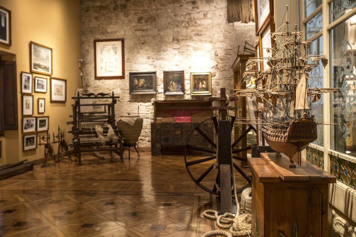 Hash Marihuana & Hemp Museum Barcelona: Skip The Line Ticket Museum room with wooden floor, ship models, vintage furniture, maritime artifacts, and framed paintings on a stone wall.