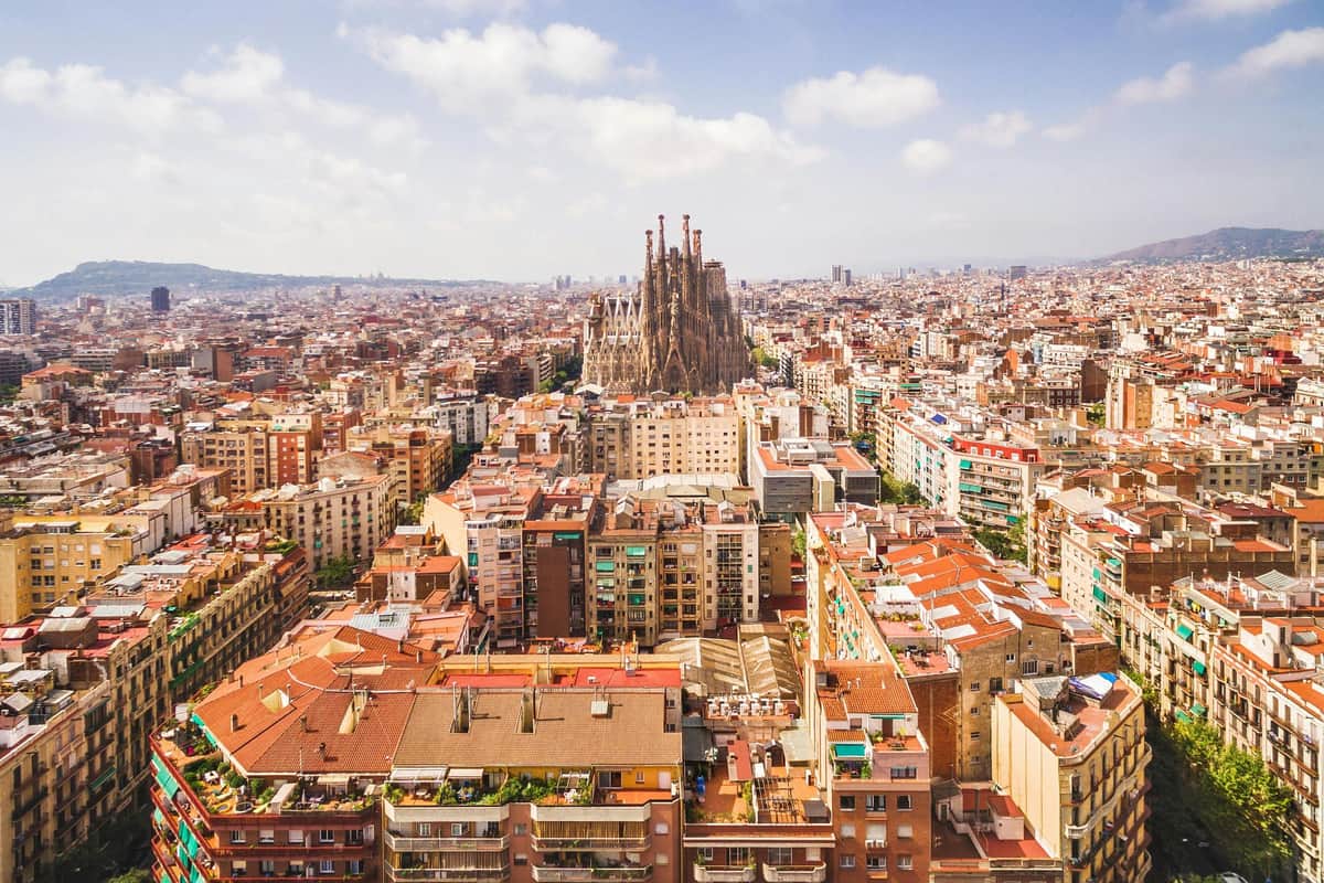 Sagrada Familia: Skip The Line Ticket + Guided Tour Aerial view of a densely packed cityscape with a large, distinctive cathedral in the center, under a partly cloudy sky.