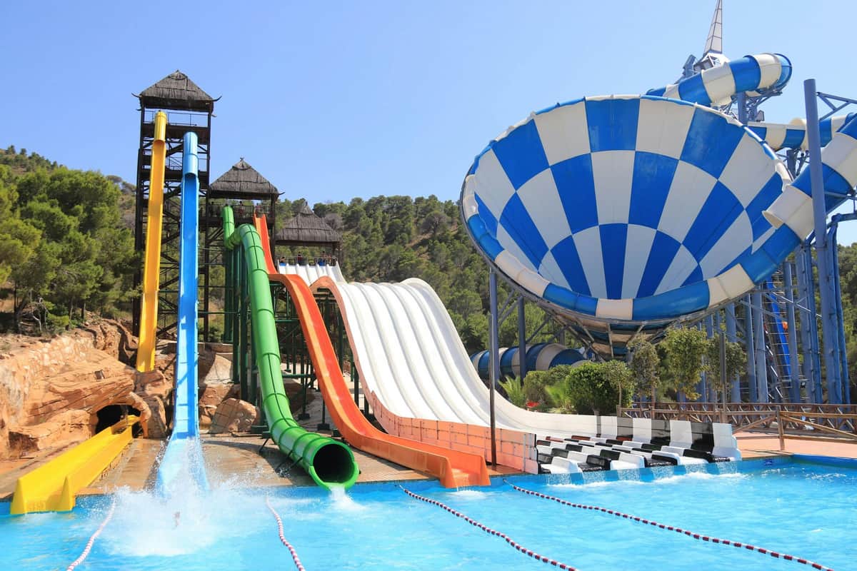 Aqualandia Benidorm: Full-Day Ticket Colourful water slides and a giant funnel-shaped water ride at a water park, with a pool in the foreground and trees in the background.