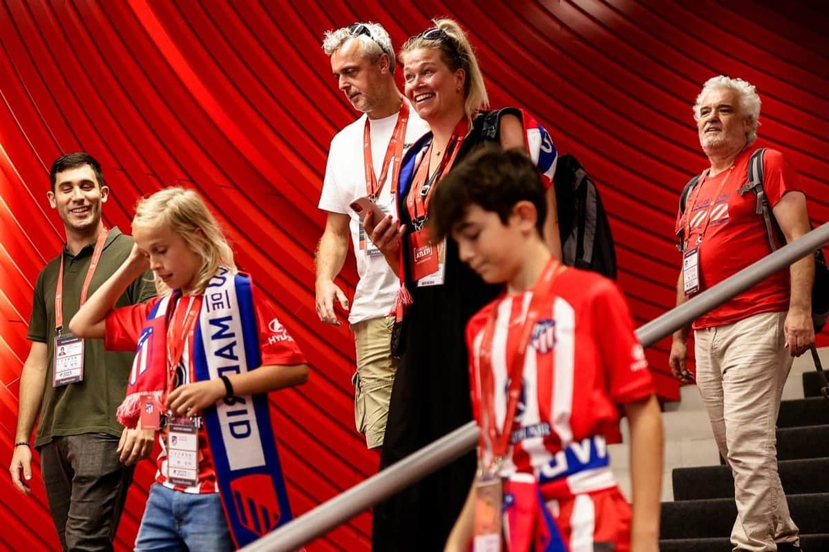 Atlético de Madrid: Skip The Line Ticket + Guided Tour + Museum Entry A family in red and white football shirts and scarves descends stairs inside a stadium with a red wall background.