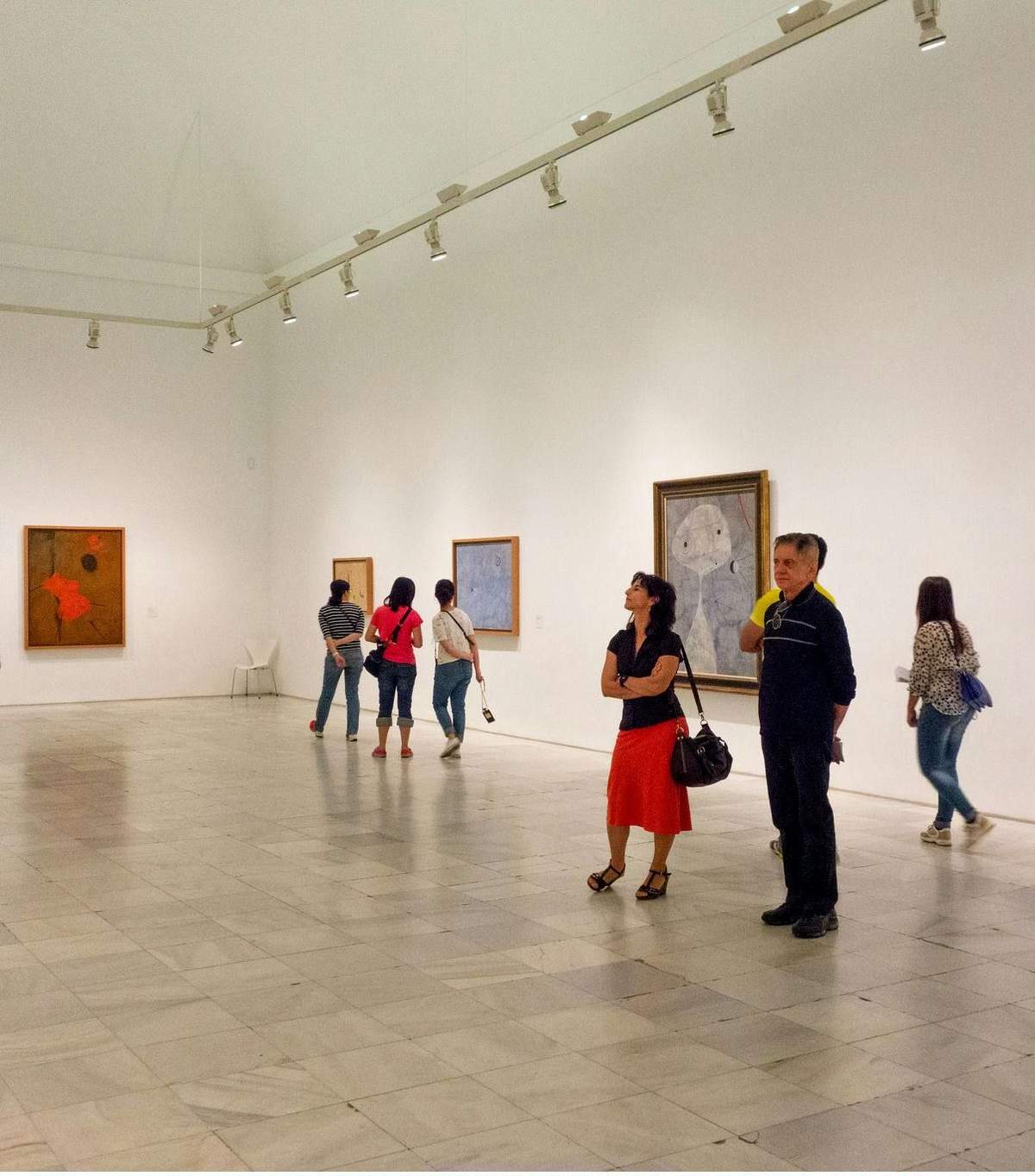 Museu Reina Sofía: bilhete sem filas + tour guiado Pessoas a observar vários quadros numa galeria de arte espaçosa, de paredes brancas, com iluminação de carris e chão de mármore.