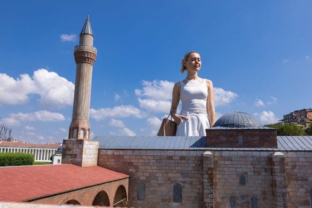 Miniatürk Museum: Entry Ticket A woman in a white dress stands behind a model of a brick building with a dome, under a clear blue sky.