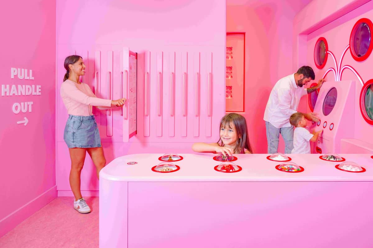 Museum of Ice Cream Miami: VIP Skip The Line Entry + Drink A young girl interacts with objects on a pink counter. A woman opens a cabinet; a man and child stand nearby. All in a pink room.