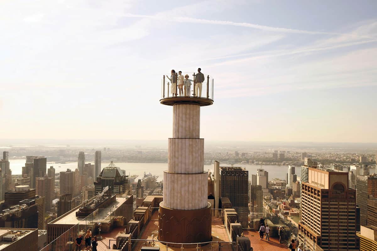 People standing on an elevated viewing platform atop a tall building, overlooking a cityscape with numerous skyscrapers and a river.