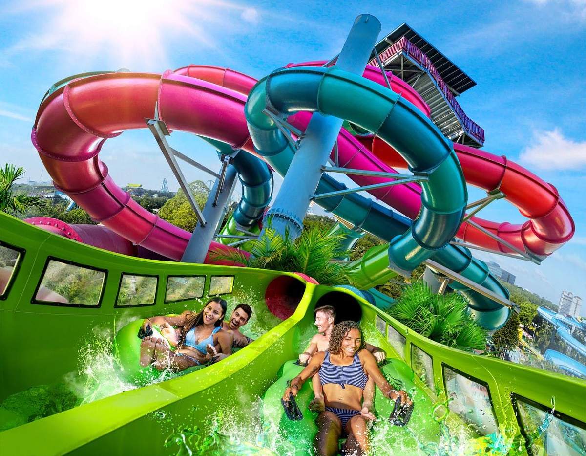 Aquatica Orlando: Fast Track Ticket Four people descending a green waterslide with intertwined red, blue, and purple slides in the background under a clear blue sky.