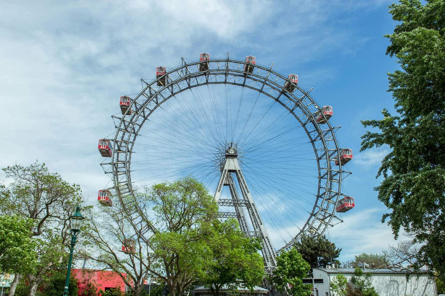 Wiener Riesenrad A large Ferris wheel with red gondolas, surrounded by trees, under a partly cloudy blue sky.