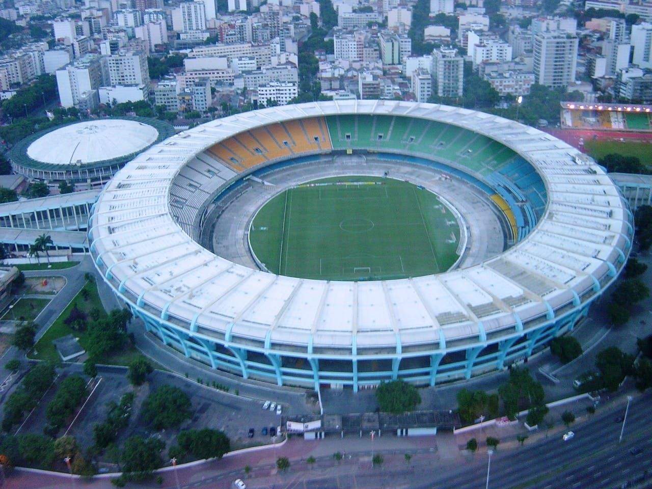 Aerial view of a large, circular stadium with a green field, surrounded by buildings and roads.