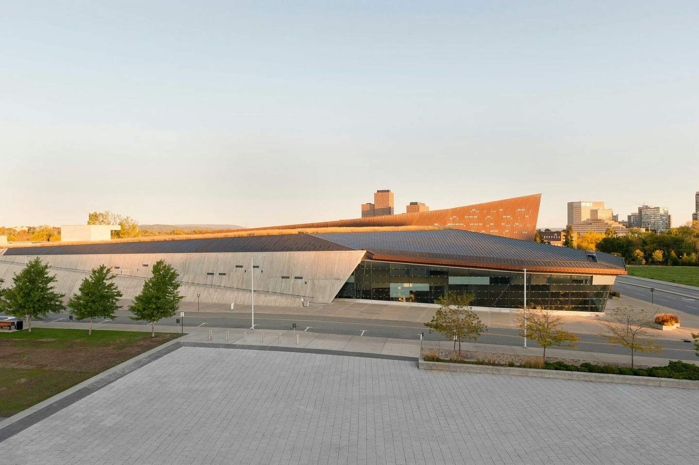 Canadian War Museum A modern building with a slanted roof, large windows, and an adjacent plaza with trees. City skyline in the background.