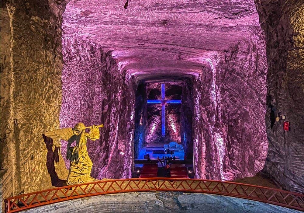 Podziemna katedra z neonowym krzyżem, posąg Jezusa z krzyżem i ławki ustawione w przejściu.