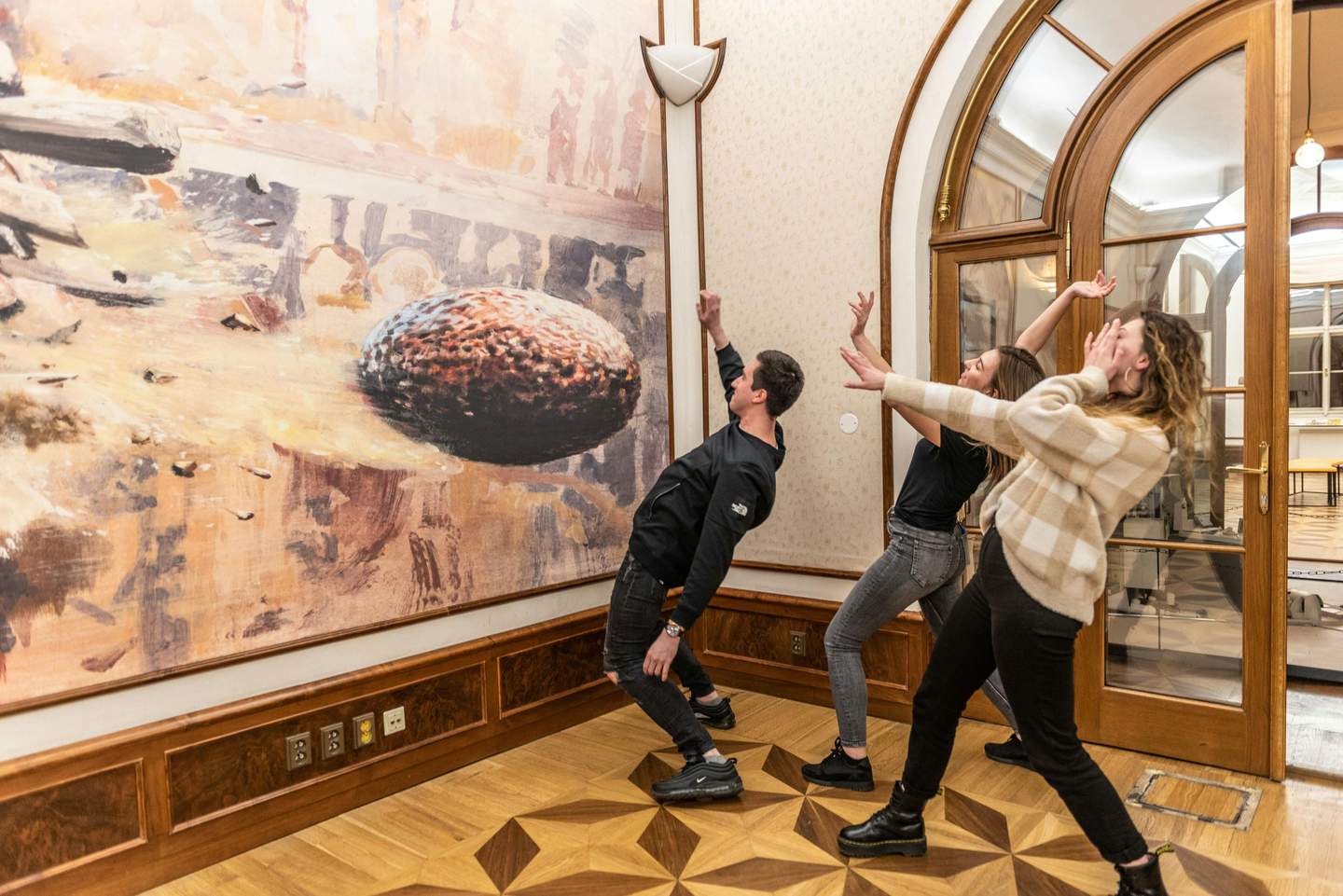 IAM Illusion Art Museum Prague Three people mimic a dramatic pose in front of a large art piece depicting a rock or meteor in an indoor gallery.