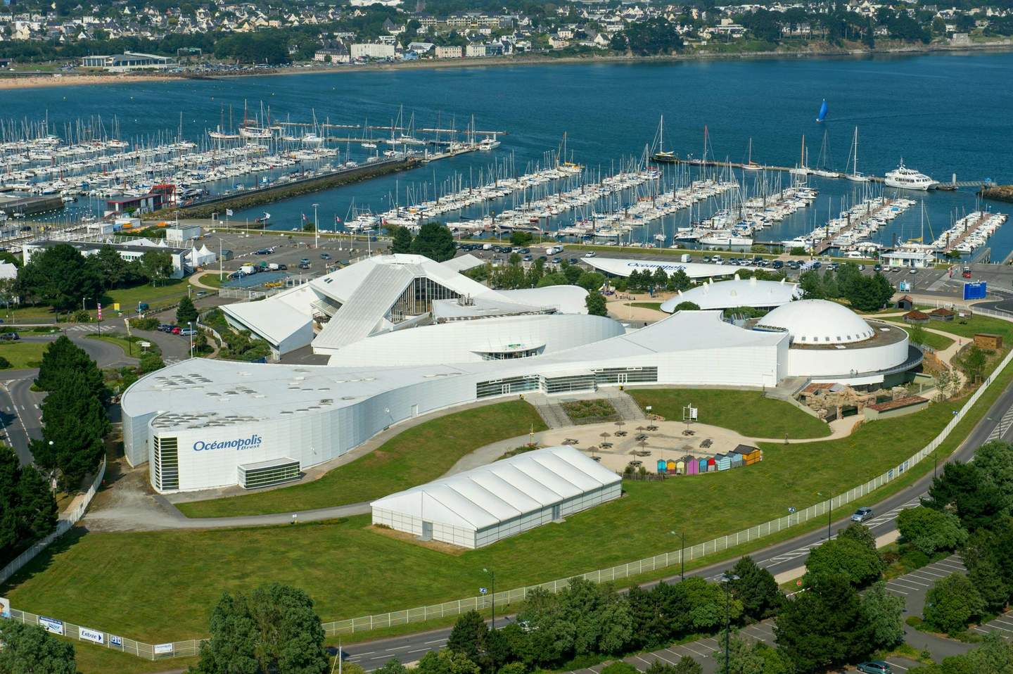 Aerial view of Océanopolis, a coastal complex with white buildings and a marina filled with boats, set by the water.