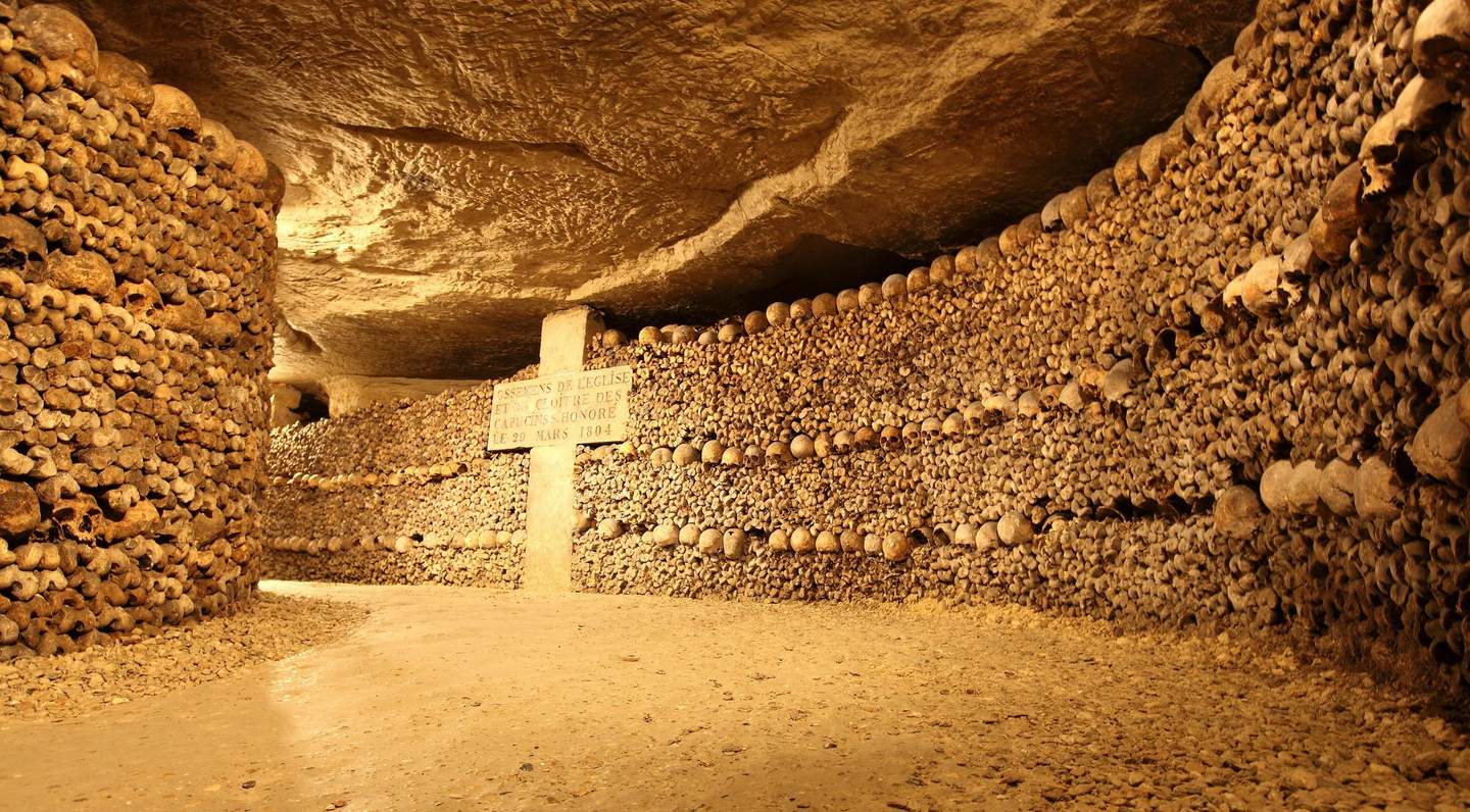 Catacombs of Paris A tunnel with walls constructed from stacked human bones and skulls, with a stone pillar displaying an inscription.