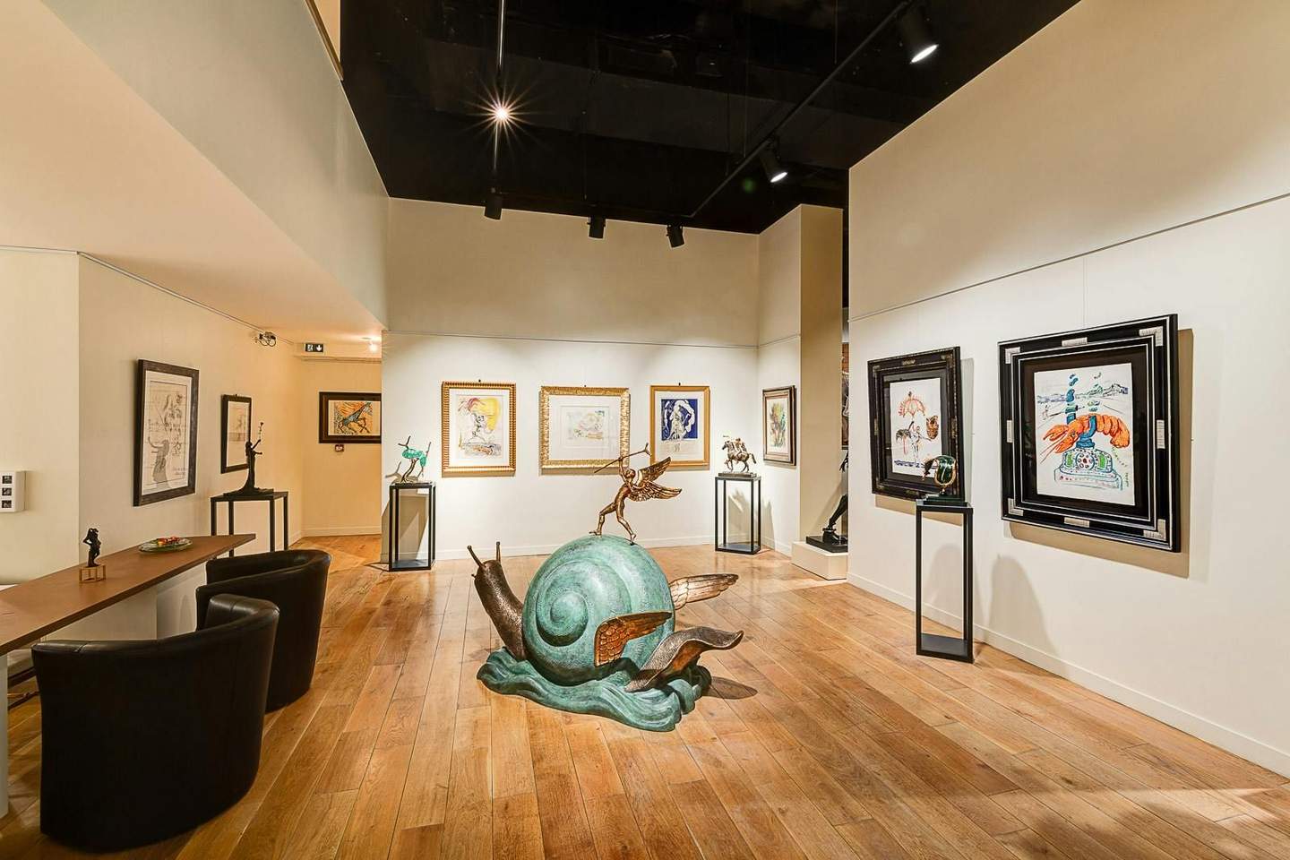 Art gallery featuring large green snail sculpture with wings, framed artworks on walls, and various sculptures on display stands.