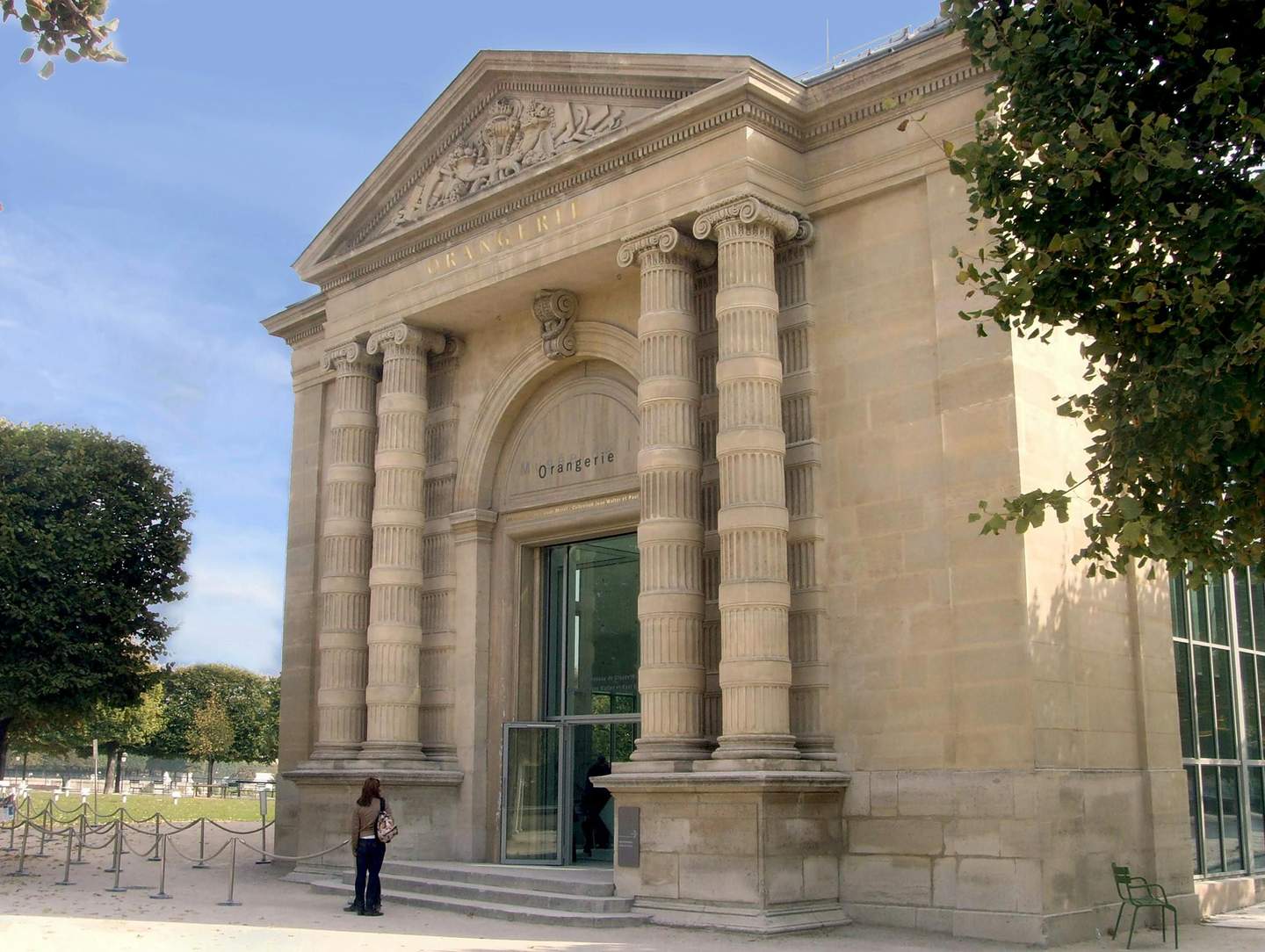 Musée de l'Orangerie An ornate stone building with large columns and "Orangerie" inscribed above the entrance. One person stands near the door.