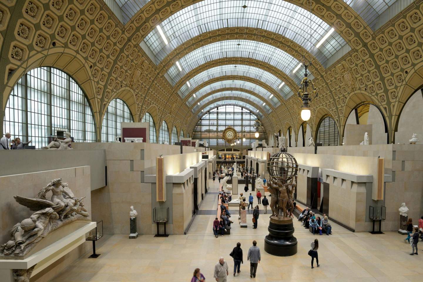 Musée d'Orsay A spacious museum hall with a vaulted glass ceiling, sculptures, and visitors walking and seated on benches.