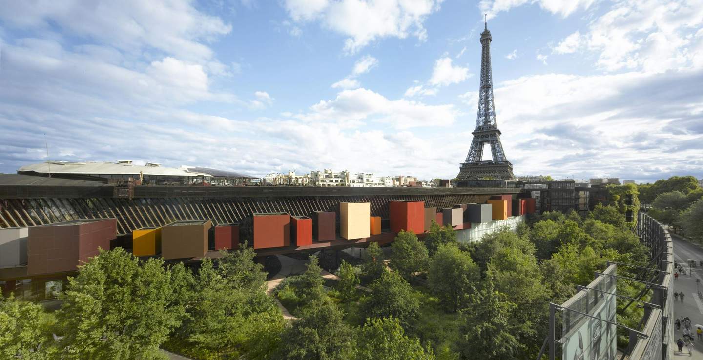 Musée du quai Branly - Jacques Chirac Colorful block-shaped buildings surrounded by lush green trees, with the Eiffel Tower visible in the background under a partly cloudy sky.
