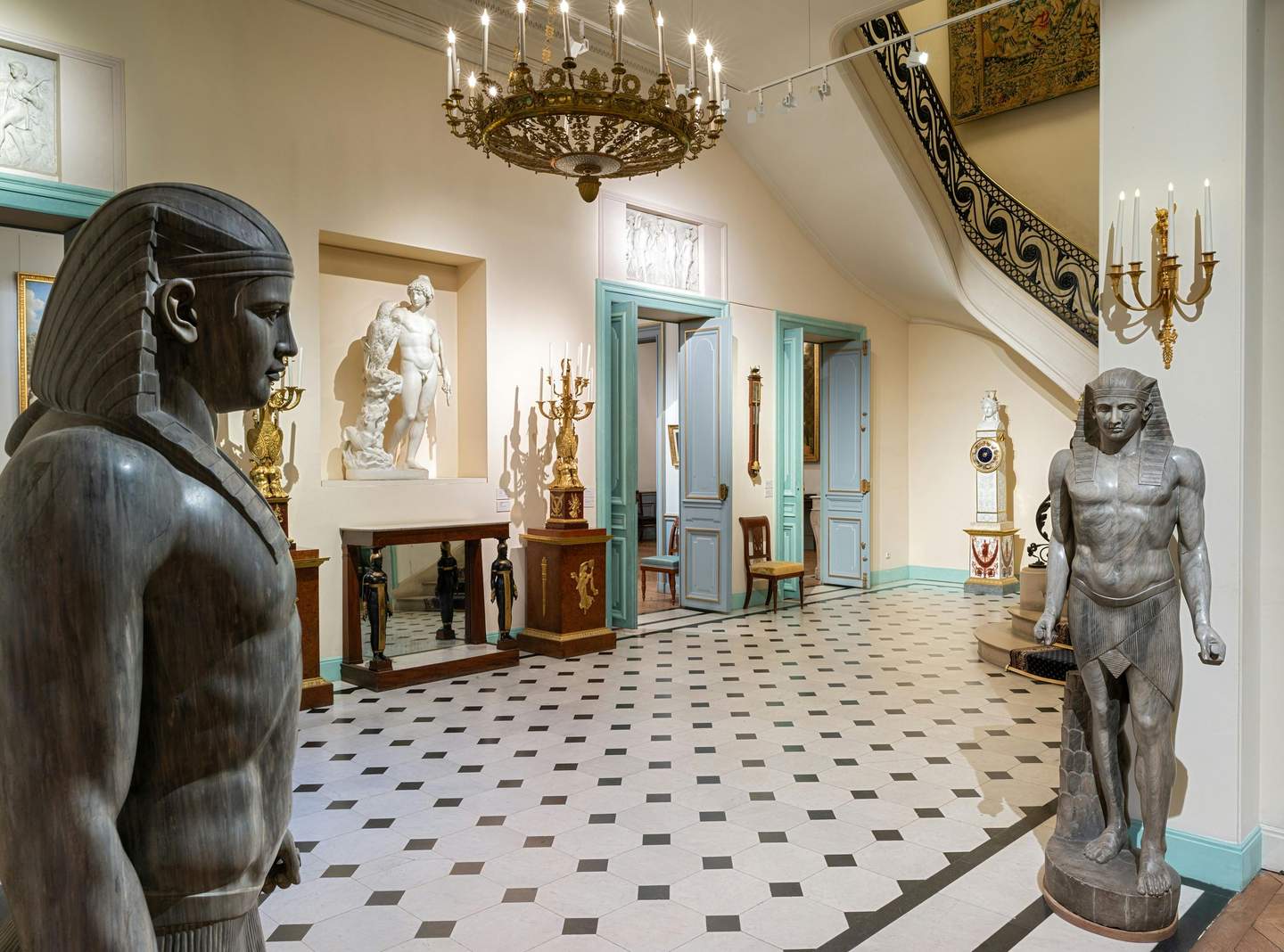 Musée Marmottan Monet Museum interior with Egyptian statues, classical sculptures, ornate chandeliers, and antique furniture in a tiled room with pale blue doors.