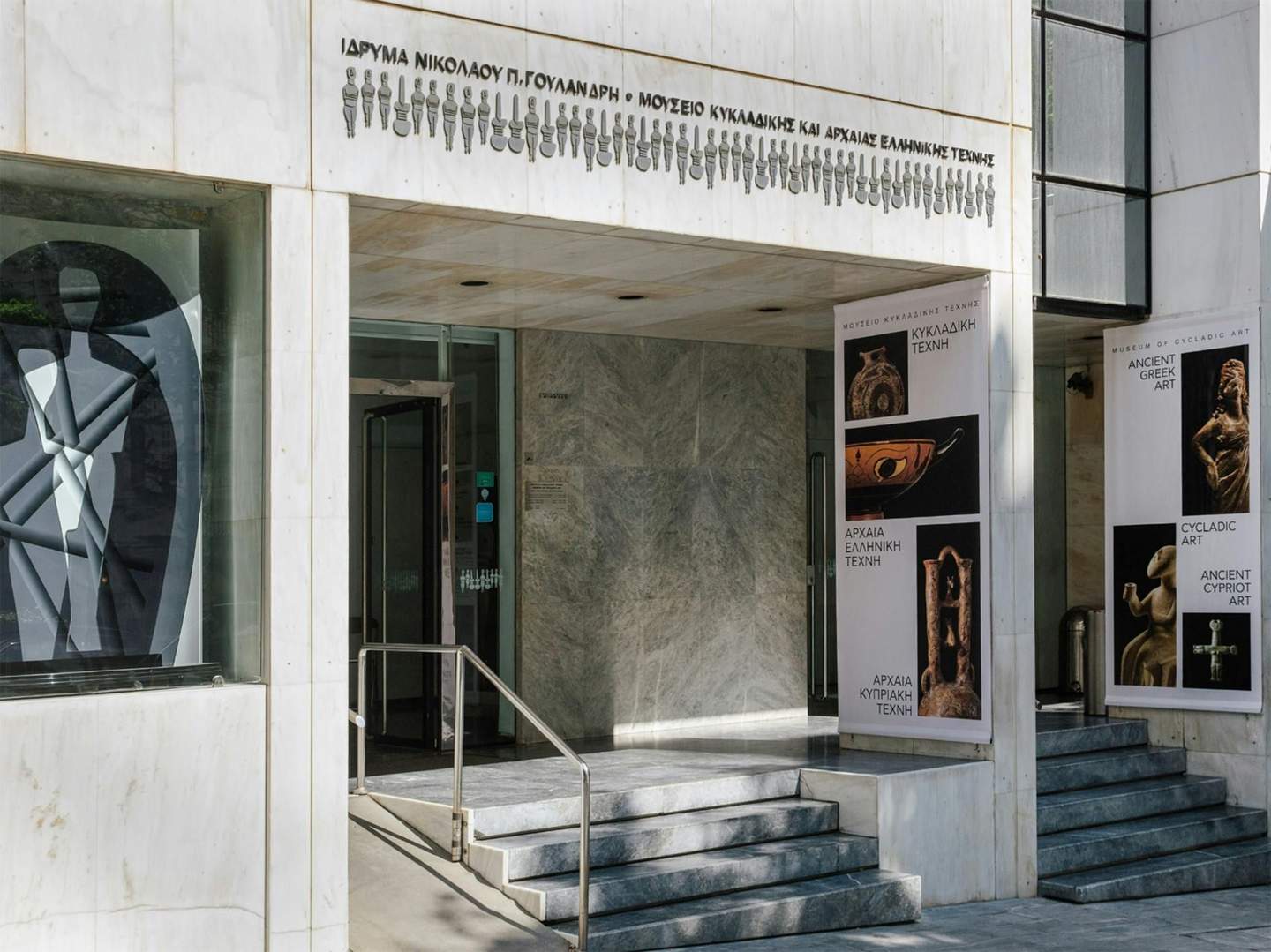 Entrance of Museum of Cycladic Art with marble steps, banners of Ancient Greek and Cypriot art, modern sculpture in the window.