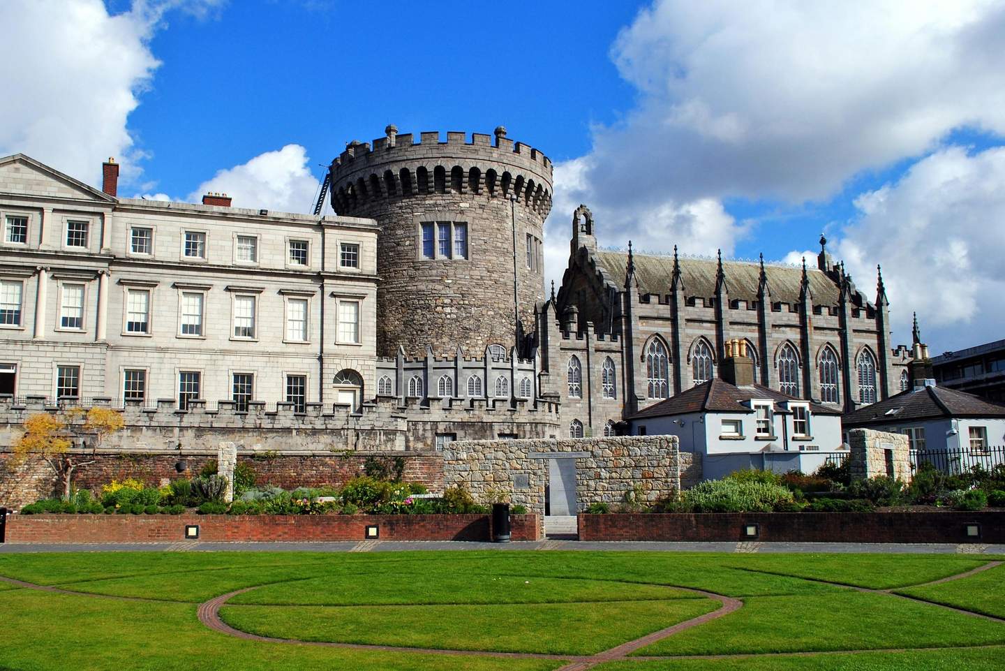 Dublin Castle Historic stone building with a round tower, gothic-style architecture, and manicured lawn under a partly cloudy blue sky.