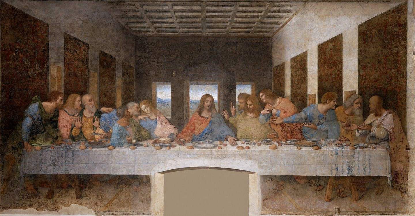 A group of people sit and stand around a long table, gesturing and conversing, with a central figure in the middle.