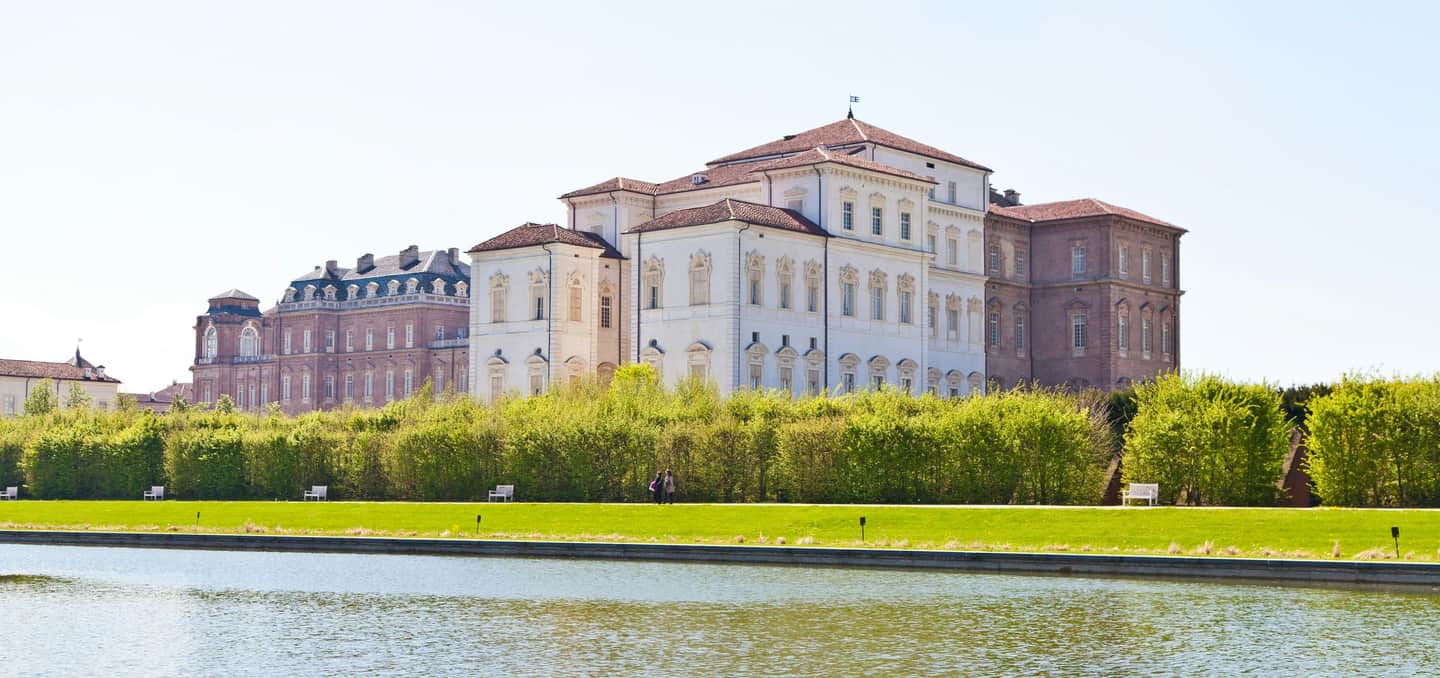 Palace of Venaria Reale Large historical building with red and white walls, surrounded by green hedges and a large water feature in the foreground.