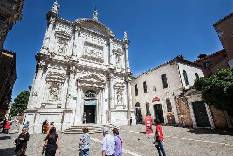 Leonardo da Vinci Museum Venice People walk outside an ornate, historical white building with statues and carvings in a sunny plaza, with a clear blue sky above.