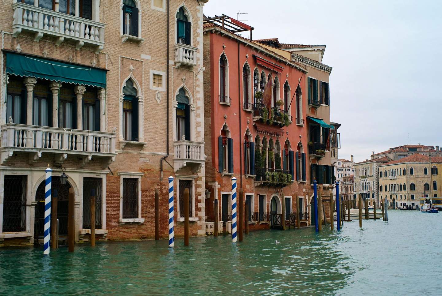 Mocenigo Palace-Museum Colorful buildings line a canal in Venice, with striped blue and white mooring poles, balconies, and arched windows.