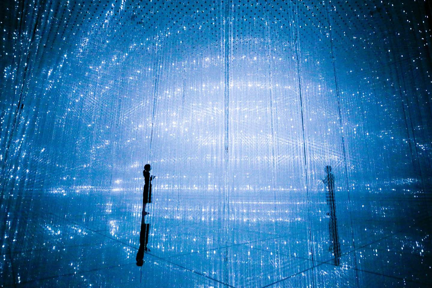 A silhouetted person stands amidst an immersive light installation with countless hanging blue LED lights.